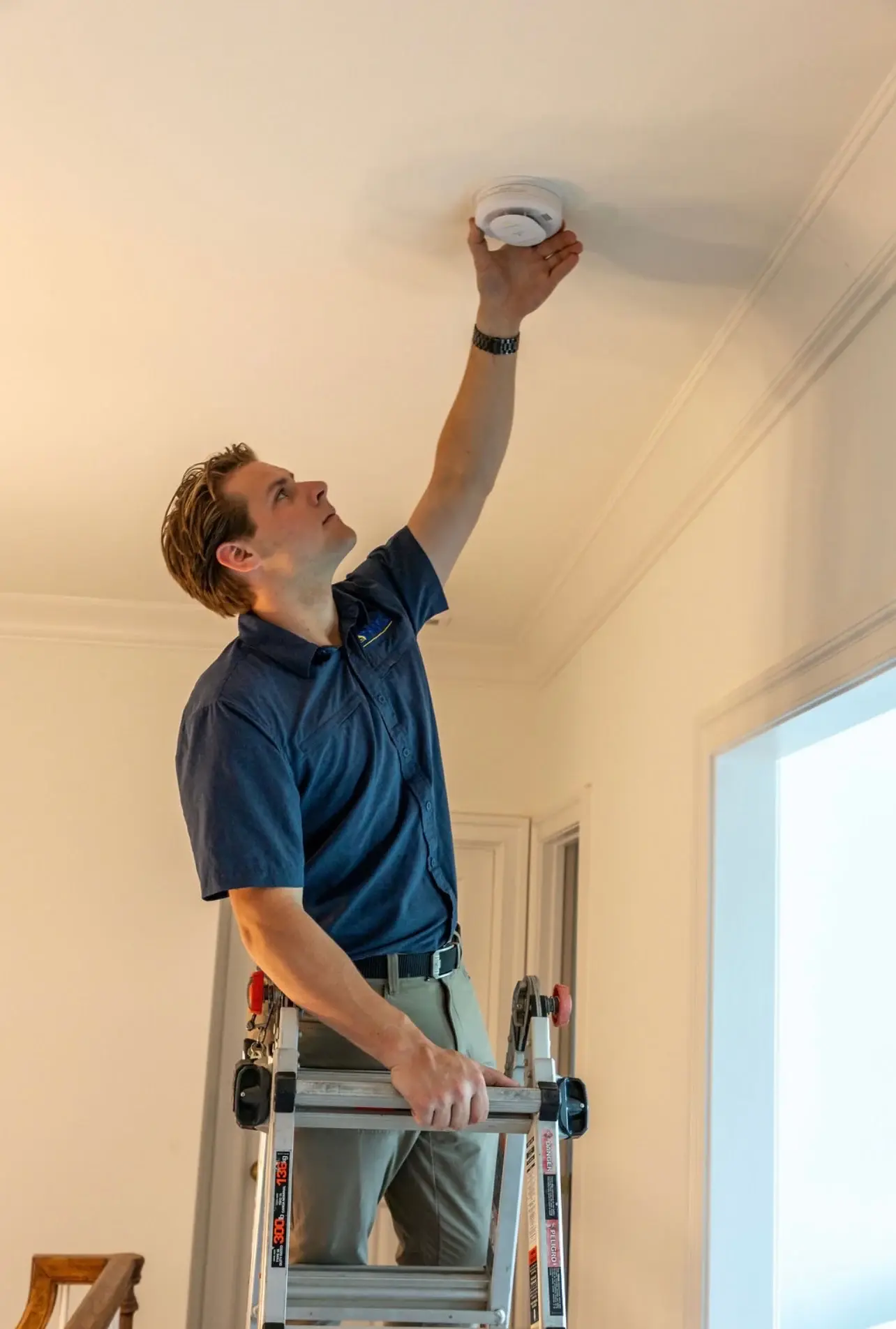 PMG technician on a step ladder testing a ceiling smoke detector